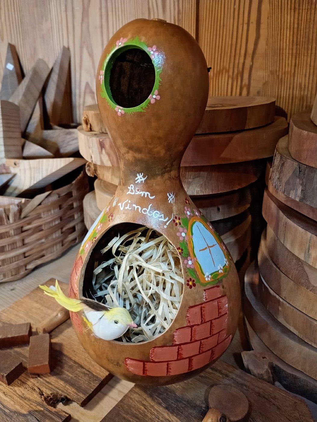 Casinha de passarinho de cabaça em tons naturais, com detalhes florais e passarinho amarelo saindo do ninho